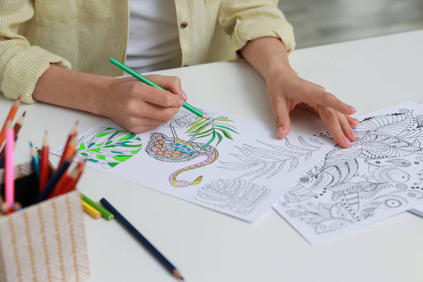 Young woman coloring antistress page at table indoors, closeup - Foto, Bild