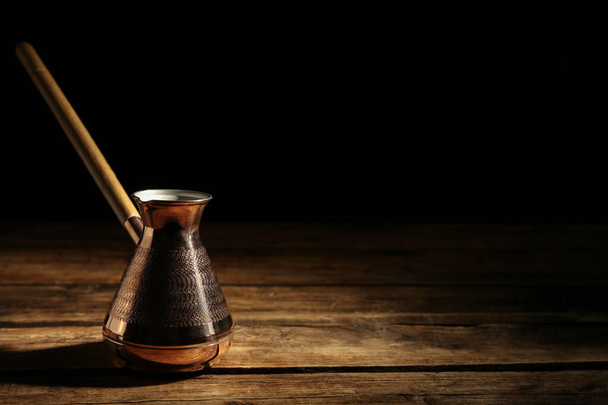Hermosa cafetera turca de cobre sobre mesa de madera sobre fondo oscuro, espacio para texto - Foto, imagen
