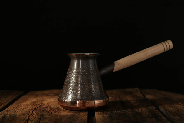 Beautiful copper turkish coffee pot on wooden table against dark background - Foto, imagen