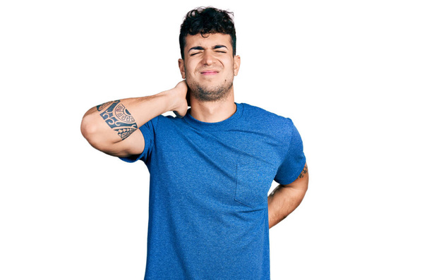 Jeune homme hispanique portant un t-shirt décontracté souffrant d'une blessure au cou, touchant le cou avec la main, douleur musculaire  - Photo, image