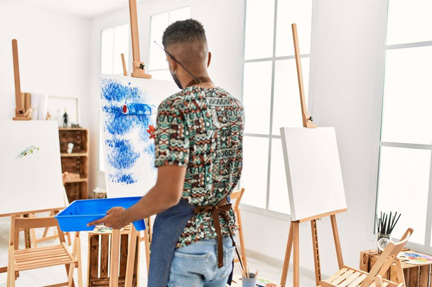 Молодий афроамериканець на задньому плані розглядає живопис з роликом на художній студії.. - Фото, зображення