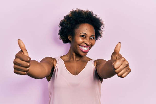 Young african american woman wearing casual sleeveless t shirt approving doing positive gesture with hand, thumbs up smiling and happy for success. winner gesture.  - Photo, Image