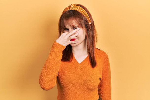 Kızıl saçlı, turuncu süveter giyen genç bir kadın pis ve iğrenç bir koku alıyor. Nefesini burnu havada tutuyor. Kötü kokuyor.  - Fotoğraf, Görsel