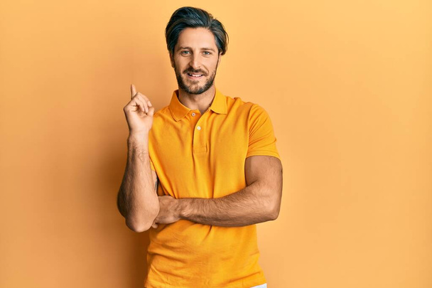 Young hispanic man wearing casual yellow t shirt with a big smile on face, pointing with hand and finger to the side looking at the camera.  - Fotó, kép