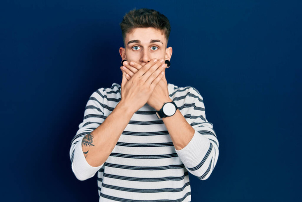 Young caucasian boy with ears dilation wearing casual striped shirt shocked covering mouth with hands for mistake. secret concept.  - Photo, Image