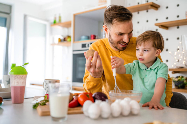 Young happy single father with a toddler boy having fun and preparing healthy food in kitchen at home. - Zdjęcie, obraz
