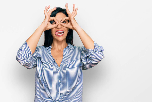 Young caucasian woman wearing casual clothes doing ok gesture like binoculars sticking tongue out, eyes looking through fingers. crazy expression.  - Fotoğraf, Görsel