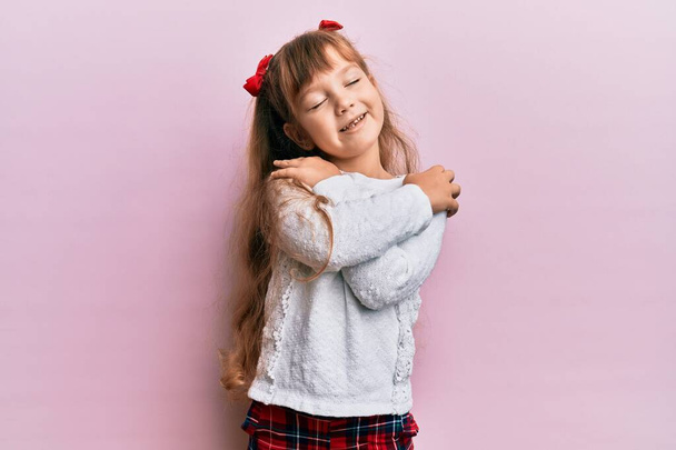 Mały biały dziewczynka dziecko nosząc casual ubrania przytulając się szczęśliwy i pozytywny, uśmiechnięty pewny siebie. miłość własna i opieka własna  - Zdjęcie, obraz