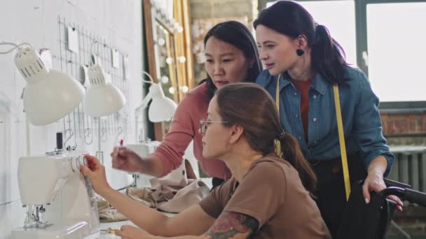 Foto vista lateral da costureira feminina usando máquina de costura e falando com designers de moda feminina em estúdio - Filmagem, Vídeo