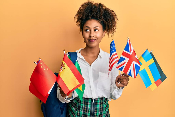 Güzel Afrikalı Amerikalı kadın afro saçlı değişim öğrencisi elinde bayraklar, gülümseyen bayraklarla yan tarafa bakıyor ve şöyle düşünüyor:.  - Fotoğraf, Görsel