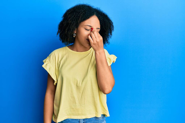 Jeune fille afro-américaine portant des vêtements décontractés fatigué se frottant le nez et les yeux ressentant fatigue et maux de tête. concept de stress et de frustration.  - Photo, image