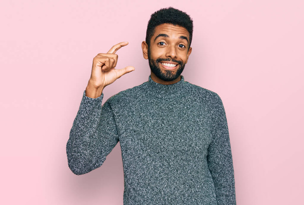 カジュアルな服を着た若いアフリカ系アメリカ人男性が笑顔で、指を見てカメラで小さなサイズの看板を手で自信を持ってジェスチャーをしています。概念を測定し.  - 写真・画像
