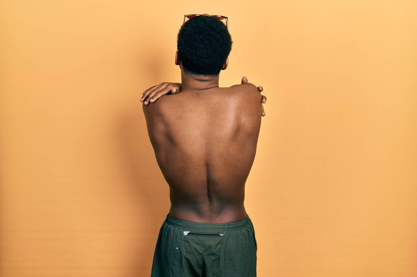 Young african american man wearing swimwear and swimmer glasses hugging oneself happy and positive from backwards. self love and self care  - Fotoğraf, Görsel