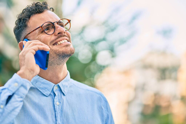 Młody latynoski biznesmen uśmiechnięty szczęśliwy rozmawiając przez smartfona w mieście. - Zdjęcie, obraz