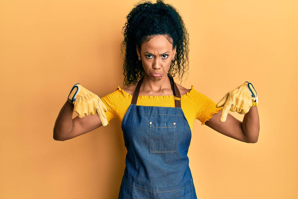 Middle age african american woman wearing professional apron pointing down looking sad and upset, indicating direction with fingers, unhappy and depressed.  - Fotografie, Obrázek