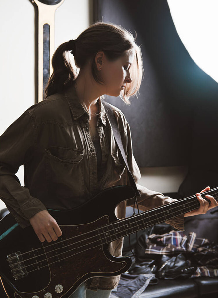 若い女性がスタジオでベースギターを弾いています。ロック・ミュージシャンのリハーサル室。録音と確認 - 写真・画像