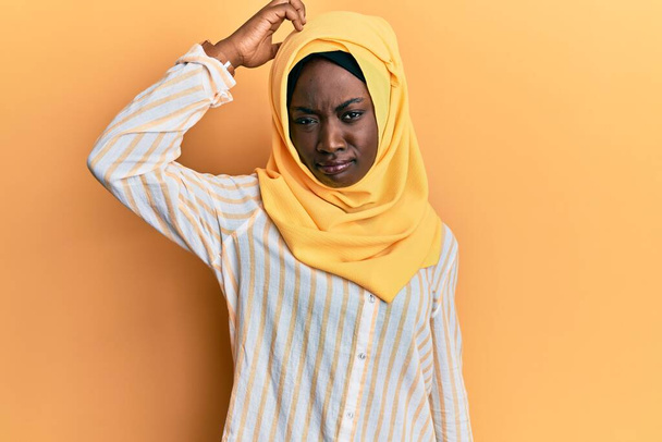 Schöne junge afrikanische Frau mit traditionellem islamischen Hijab-Schal verwirrt und fragt sich, was das soll. Unsicher im Zweifel, mit der Hand auf dem Kopf denkend. Nachdenkliches Konzept.  - Foto, Bild