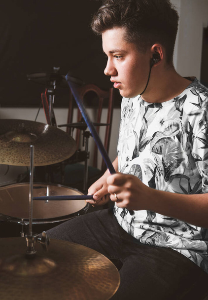 handsome teenager boy drummer playing on rehearsal in a studio. rock musician male teen performing a song. hobby and leisure concept. vertical size - Zdjęcie, obraz