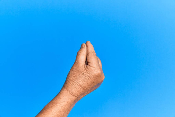 Ruka staršího hispánského muže přes modré izolované pozadí držící prázdné místo palcem prst, podnikání a reklama  - Fotografie, Obrázek