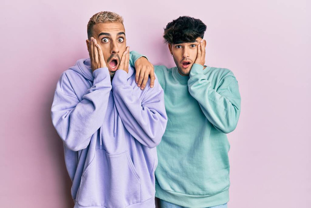 Homoseksueel gay paar staan samen dragen casual kleding bang en geschokt, verrassing en verbaasd uitdrukking met handen op gezicht  - Foto, afbeelding