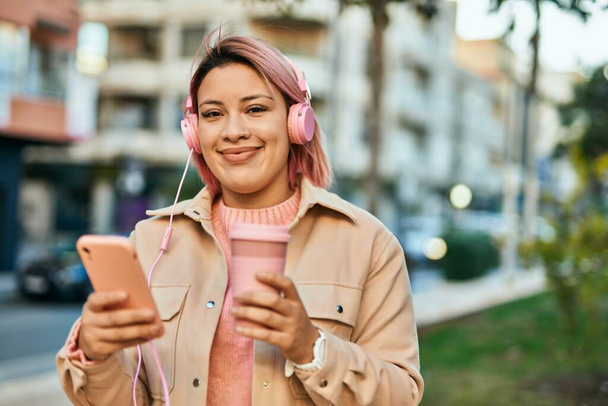 Young hispanic girl drinking coffee using smartphone and headphones at the city. - Foto, immagini