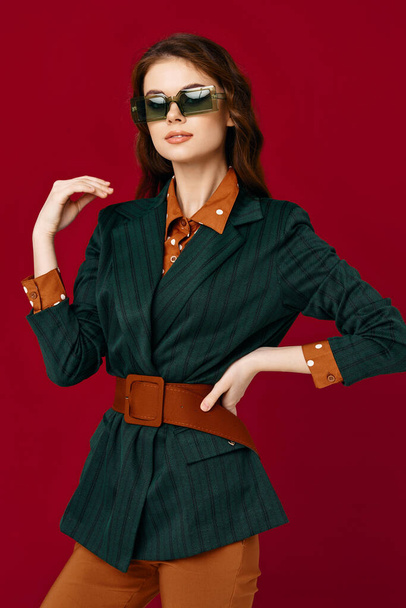 Brünette trägt Sonnenbrille Jacke Mode Kleidung posiert rotem Hintergrund - Foto, Bild