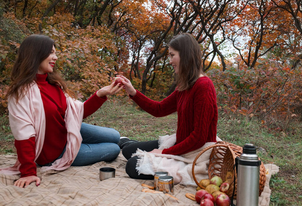 Šťastná dospělá žena pije čaj s mladou dcerou v lese za teplého podzimního dne. útulný teplý podzimní den, příjemné chvíle s příbuznými v přírodě - Fotografie, Obrázek
