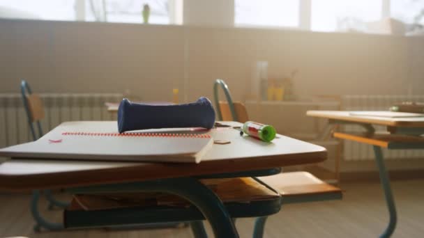 Iskolai kellékek hevernek az asztalon az osztályteremben. Jegyzetfüzet és tolltartó az asztalon - Felvétel, videó