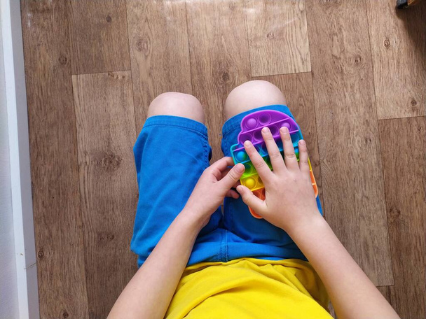Niño en pantalones cortos azules jugar con colorido juguete poppit fidget. Juguete sensorial anti-estrés para niños y adultos - Foto, imagen
