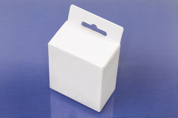 Закрытая прямоугольная коробочка с подвеской из белого картона на голубой поверхности - Фото, изображение