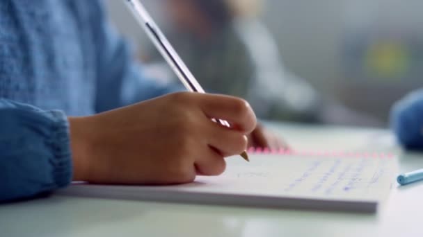 Girl writing in notebook at desk in classroom. Student doing classwork at school - Felvétel, videó