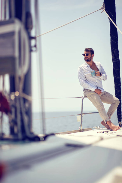 A young handsome male model is sitting on a yacht on the seaside and enjoying a photo shooting on a beautiful sunny day. Summer, sea, vacation - Valokuva, kuva