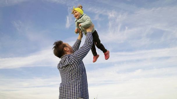 Отец и маленький ребенок играют, смеются и обнимаются вместе. Папа бросает счастливую дочь в голубое небо. Эппи семья путешествует. Ребенок на руках у родителей. Папин выходной. Концепция счастливой семьи - Фото, изображение