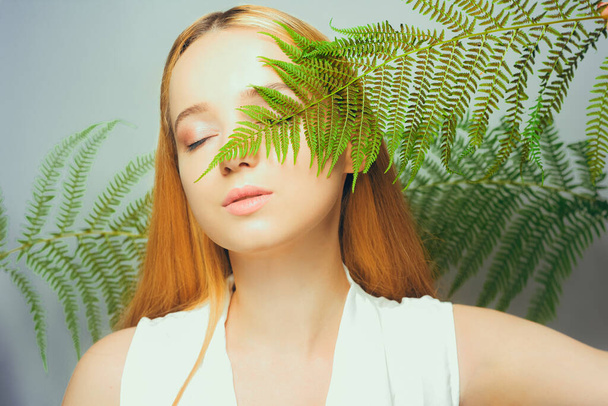 Beautiful young blond woman with perfect skin and natural make up posing front of plant tropical green leaves background. Teen model hair care of her face Fashion. - Foto, Imagem