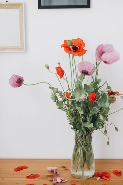 Beautiful poppies bouquet on wooden table in room. Gathering countryside wildflowers, rural still life. Red common poppy and purple opium poppy flowers in vase - Photo, Image