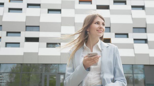 Adult Caucasian Confident Young Business Woman in White Shirt is enjoys on Phone Outside near Modern Office Building. Medium Long Low Angle 4K Slow Motion Corporate Shot with Moving Around - Foto, Imagen