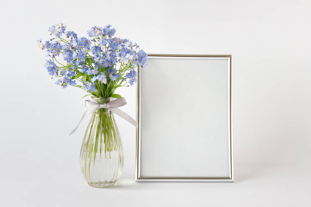 Large A4 silver frame mockup template with blue forest flowers in glass vase on the right side on white background. - Foto, imagen