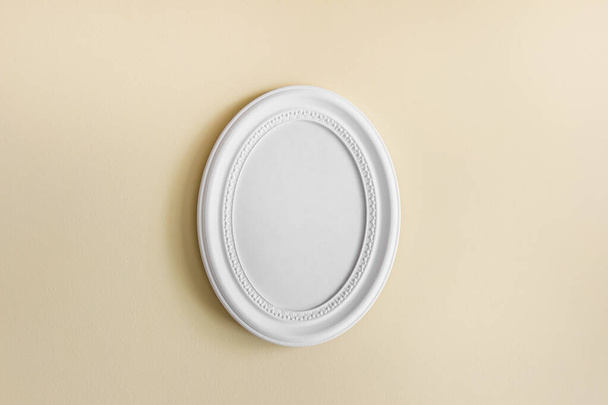 Round oval white frame with white blank oval frame on yellow textured wall. - Photo, Image