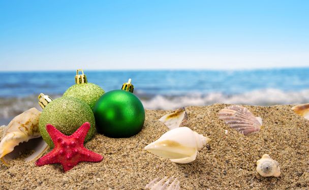 Рождественские шары и раковины на песке на фоне моря летом
  - Фото, изображение