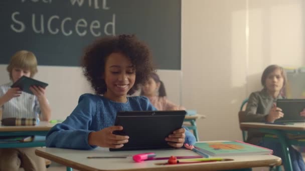 Sonriendo chica afroamericana utilizando tableta digital en clase con compañeros de clase  - Imágenes, Vídeo