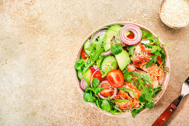 Grilled chicken salad with tomatoes, arugula, red onion, avocado, sesame seeds and lemon oil dressing. Healthy food. Beige background. Top view - Foto, Imagem