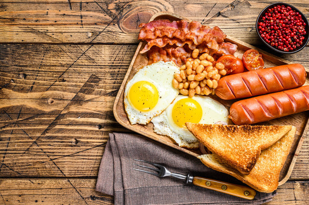 English Breakfast in a wooden tray with fried eggs, sausages, bacon, beans and toasts. wooden background. top view. Copy space - Фото, изображение