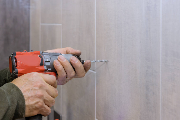 Hände des Klempners mit einem Bohrer, um neue Löcher in Fliesen Badezimmerwand für die Installation von Bad-Accessoires erstellen - Foto, Bild