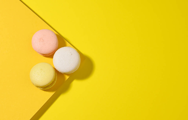 round multicolored macarons on a yellow background with a shadow on a yellow background. Gourmet almond flour dessert, top view - Foto, Imagem