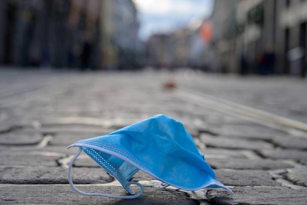 Máscara protetora azul descartável descartada em uma rua urbana vista de perto durante a pandemia de Covid-19 ou coronavírus - Foto, Imagem