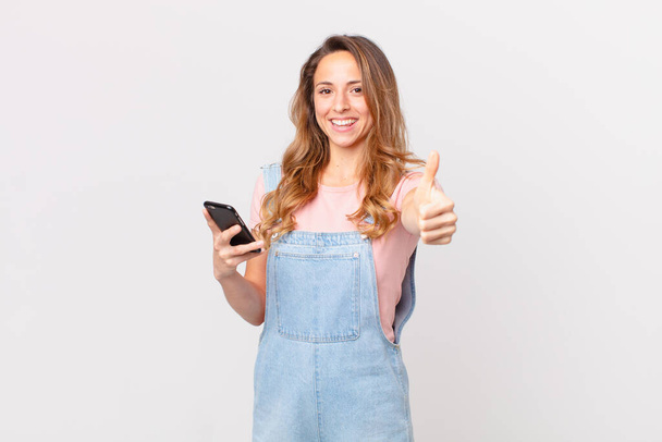 pretty woman feeling proud,smiling positively with thumbs up and holding a smartphone - Photo, Image