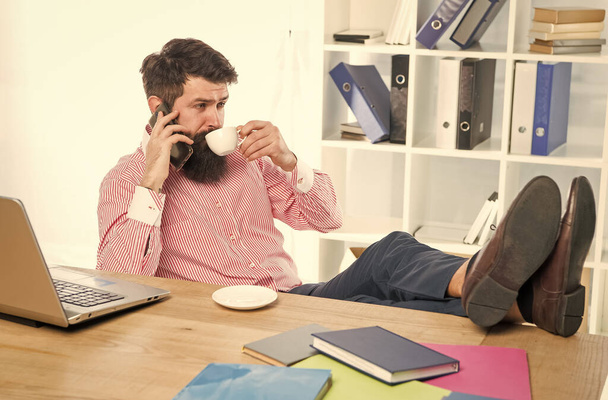 Співробітник п'є чашку чаю, розмовляючи на мобільному телефоні в сучасному офісі, технології
 - Фото, зображення
