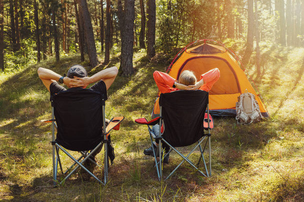 森林キャンプ場のキャンプチェアでリラックスして自然を楽しむ人たち - 写真・画像