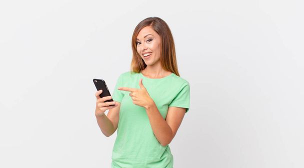pretty woman looking excited and surprised pointing to the side and using a smartphone - 写真・画像