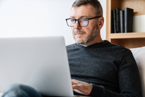 Serious adult unshaven man working with laptop while sitting at home - Photo, image